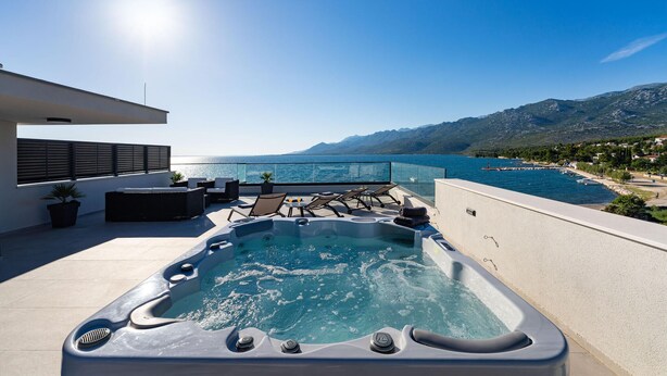 Eine Dachterrasse mit Whirlpool, Sitzgelegenheit im Freien und Blick auf Meer und Berge.