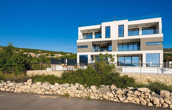A modern multi-story building with large windows and balconies, surrounded by greenery and a stone wall. - Cozy apartment in Rovanjska with WiFi (Rovanjska)