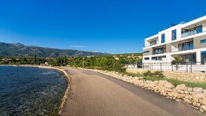 Ein modernes Gebäude mit mehreren Balkonen, das auf einen See mit Blick auf Berge und viel Grün blickt.
