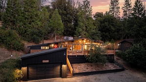 A modern house with a large garage, a wooden deck, and a staircase leading to a second level. - Family Cabin, Dog, Ht Tb, 15 min Yosemite, Valentine's Day + Firefall Packages (Oakhurst)