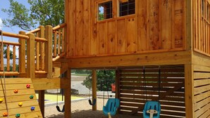 Una casetta di legno con scivolo, parete da arrampicata e altalene.