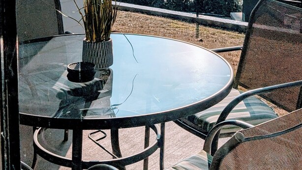 Un balcone con un tavolino e sedie in vetro, una pianta in vaso e vista su un ponte e montagne.