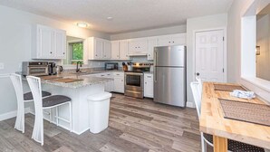 A modern kitchen with white cabinets, stainless steel appliances, and a wooden dining table. - Ocean Pines 3BR House Resort Community (Berlin)