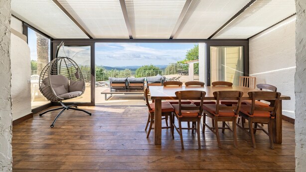 Une pièce spacieuse avec une table et des chaises en bois, un fauteuil suspendu et une vue sur l’extérieur.