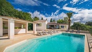 Une piscine avec des chaises longues, un patio couvert et une vue sur une villa.