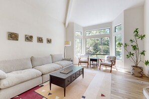 Relax in this stylish living room with a sofa, coffee table, and artwork, surrounded by natural light and a potted plant.