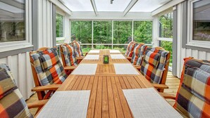 A covered patio with a wooden table and chairs, large windows, and a view of greenery. - Beautiful home in Båstad with sauna (Båstad)