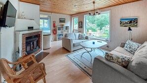 A living room with a fireplace, a sofa, a dining table, and a view of the outdoors. - Beautiful home in Båstad with sauna (Båstad)