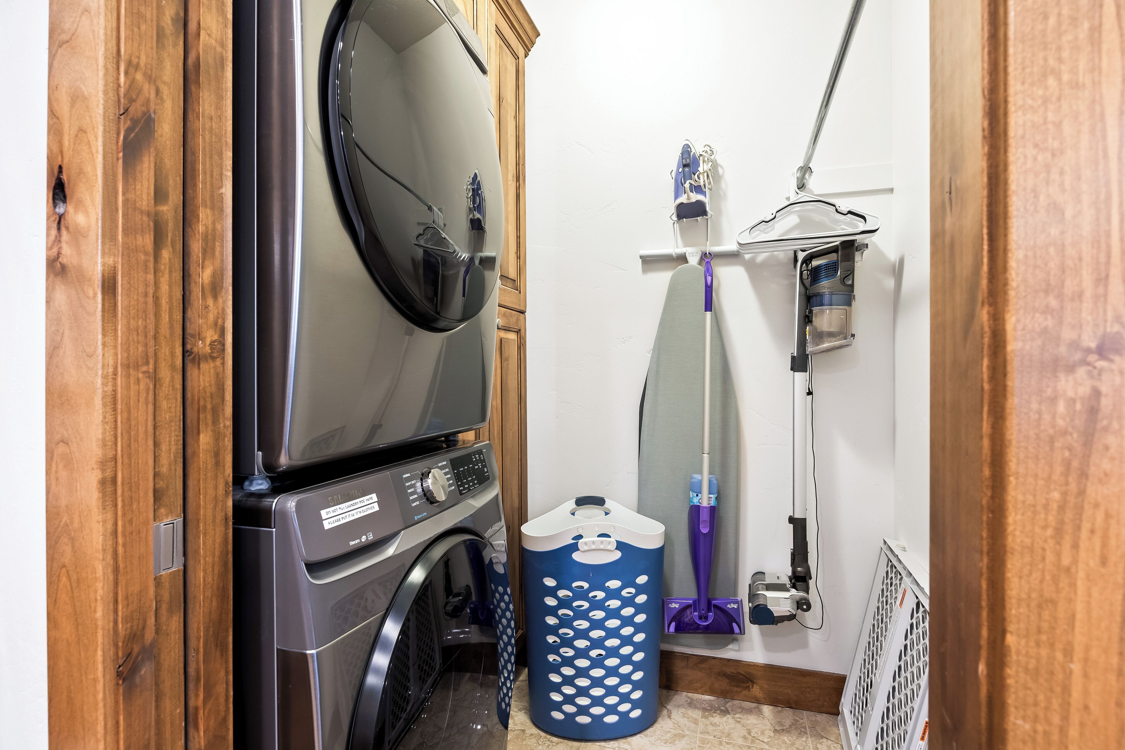 Une buanderie équipée d’un lave-linge et d’un sèche-linge à chargement frontal, d’un panier à linge bleu et d’une serpillière rangée sur un porte-balai fixé au mur.