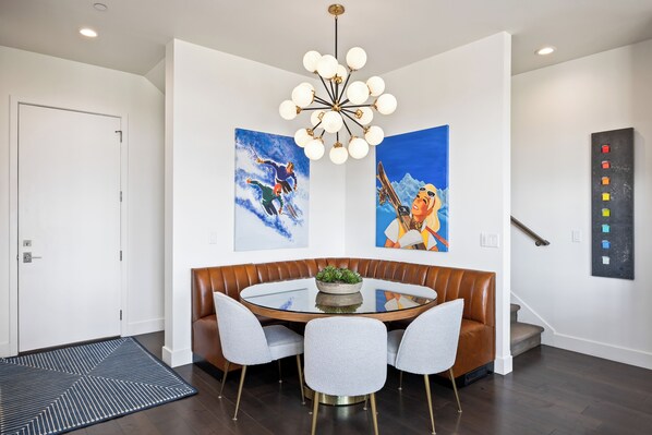 A modern dining area with a round glass table, leather booth seating, and a central plant.