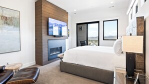 Une chambre d’hôtel moderne dotée d’un grand lit, d’une cheminée, d’un téléviseur fixé à un mur en bois et d’un balcon avec vue.