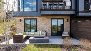 Une maison moderne à deux étages, dotée d’une façade en pierre, de grandes fenêtres et d’un balcon aménagé avec du mobilier d’extérieur.