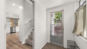 Ein Flur mit einer Treppe, die zu einer Küche führt, einer Tür mit einem Metallgitter und einem Fenster mit Blick auf Grünflächen.