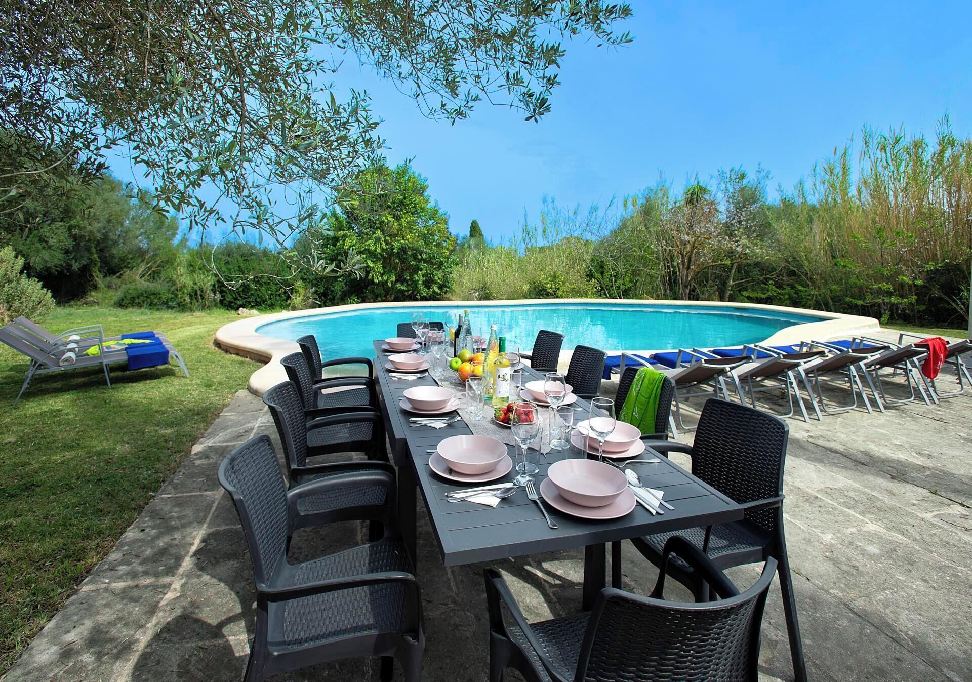 Ein Essbereich im Freien mit Pool, umgeben von Grün und mit schwarzen Stühlen und Tischen, die für eine Mahlzeit gedeckt sind.