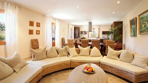 A spacious living area with a curved sofa set, a round glass coffee table, and a kitchen in the background. - Beautifully Restored Country House, A/C Private Pool, Mountain Views - 10mins to Old Town Pollenca (Pollença)