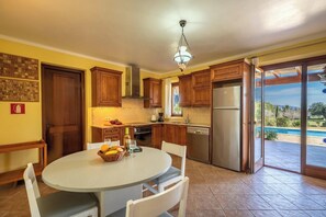 Enjoy meals in this kitchen with a dining table and chairs, a refrigerator, and a large window opening to a patio with a pool.