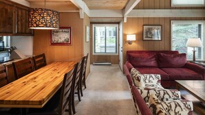Ein gemütliches Interieur mit einem Holzespeisetisch, Stühlen, einem roten Sofa und einem gemusterten Hocker.