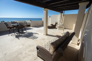 Relax in style with a comfortable seating area, wicker furniture, and a dining table, surrounded by a tranquil ocean view.