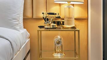 A modern hotel room with a neatly made bed, a bedside lamp, a small table with decorative items, and a glass cabinet.