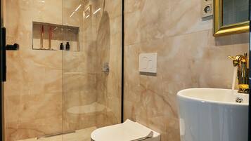 Une salle de bain moderne avec une douche à parois de verre, des toilettes blanches et un grand lavabo doté d’un robinet doré.