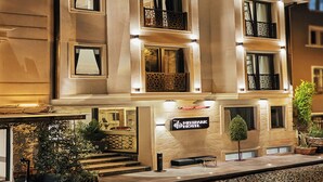 Ett hotell med en skylt som visar texten ”Mitspark Hotel”. Det har en modern fasad med balkonger, en trappa som leder till entrén och planterade blommor i krukor.