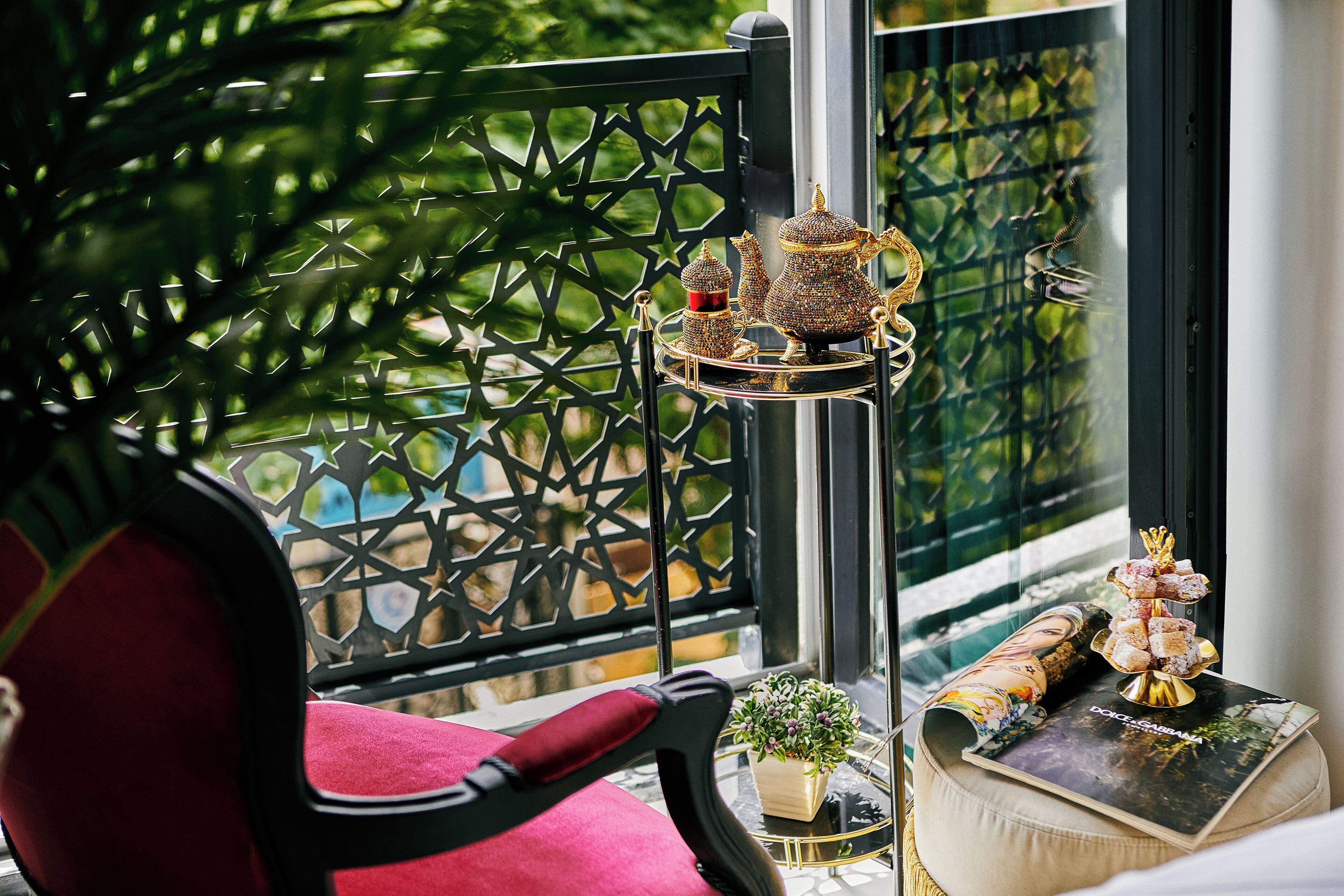 A balcony with a decorative metal fence, a chair with a red cushion, and a table with a small plant and a decorative item.