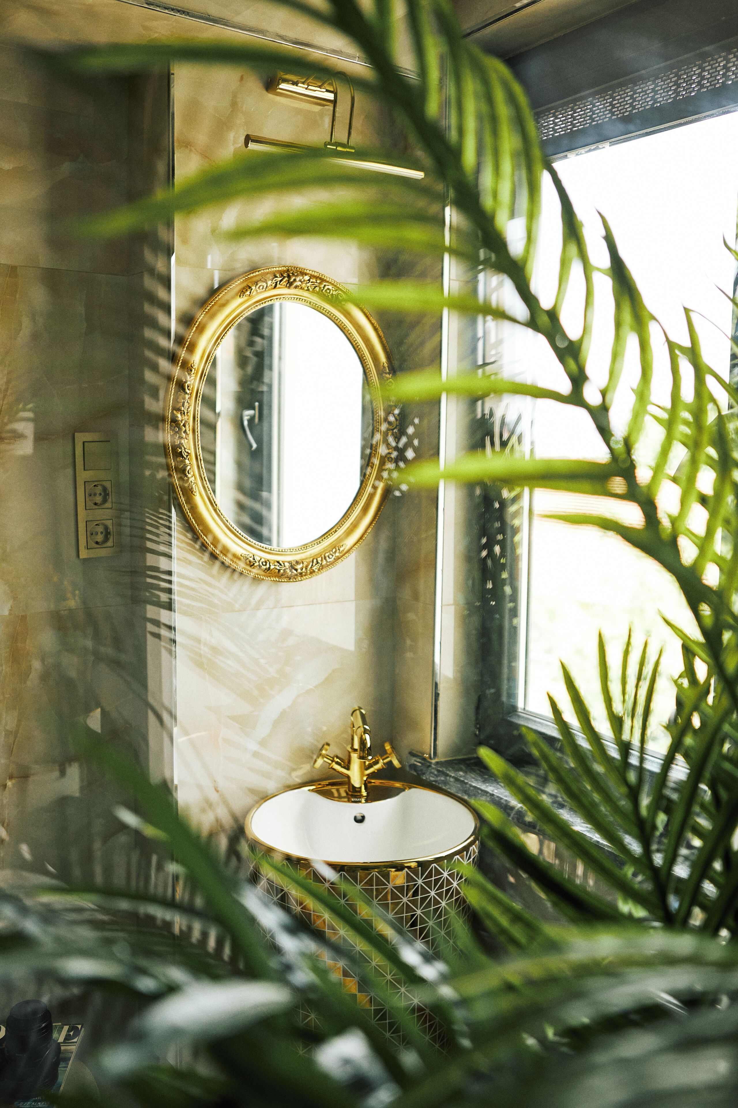 A bathroom with a gold-framed mirror, a white sink with gold accents, and a shower area.