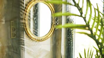 A bathroom with a gold-framed mirror, a white sink with gold accents, and a shower area.