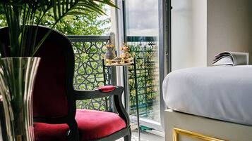 A hotel room with a bed, a red chair, a small table with a decorative item, and a large potted plant.
