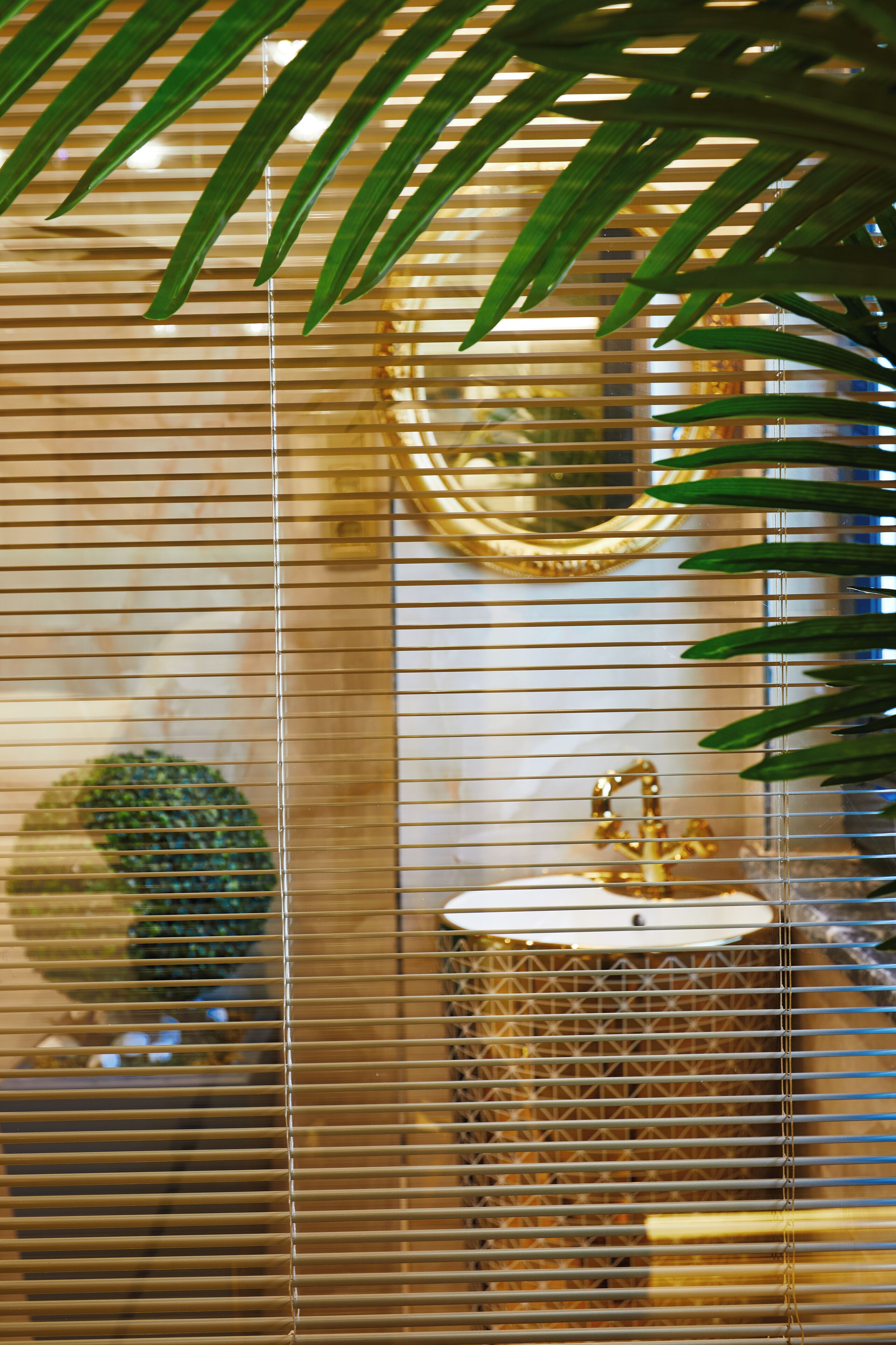 A room with a wooden blinds design, a round mirror, and a gold-colored sink.