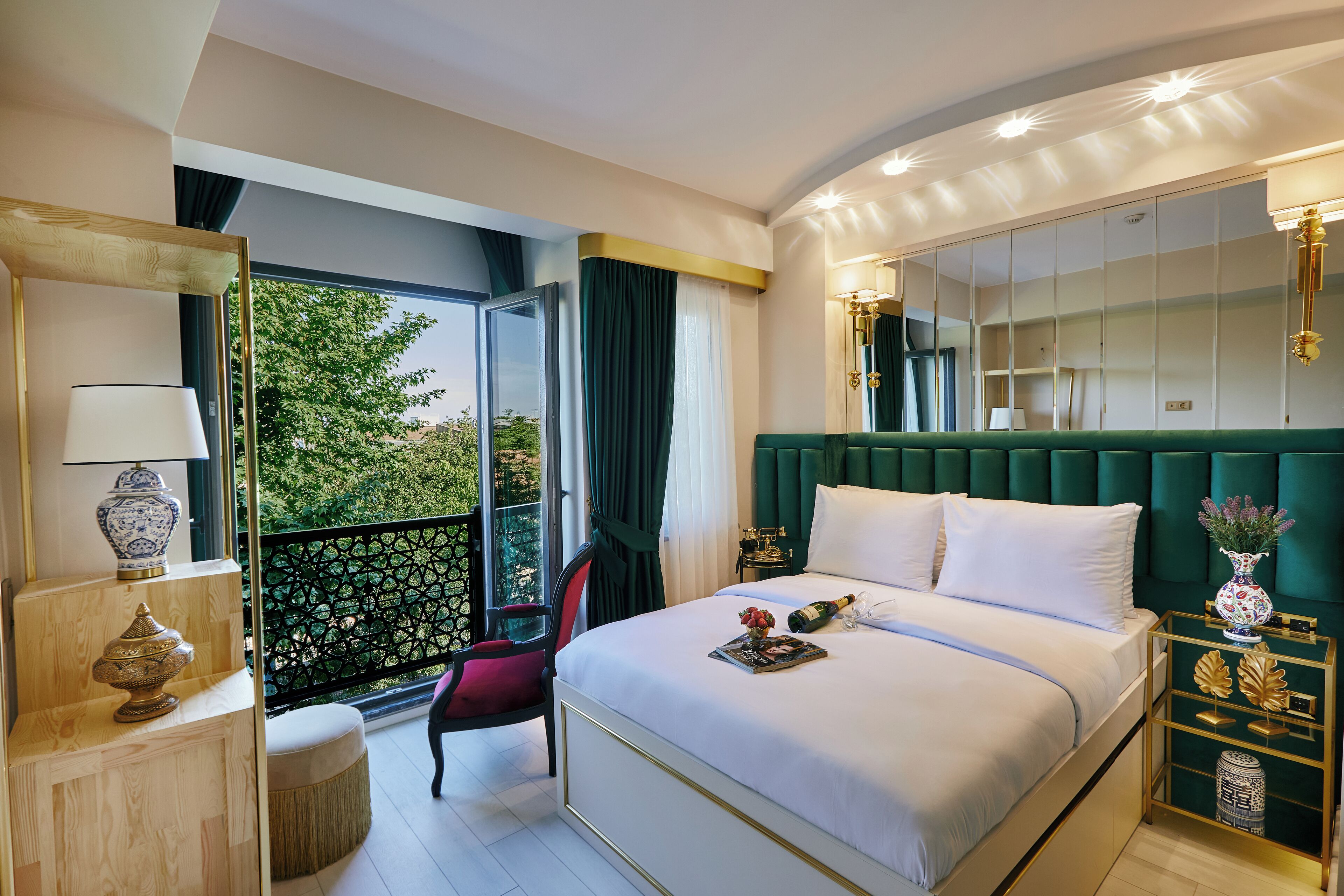 A hotel room with a large bed, a balcony with a view, a desk with a lamp, and a mirror.