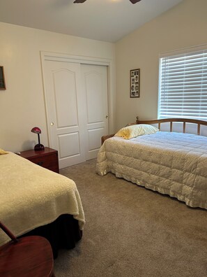 A bedroom with two beds, a wooden headboard, a bedside table with a lamp, a door, and a window with blinds. - Desert Oasis Retreat (Rio Rico)