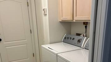 A laundry room with a front-loading washer and dryer, a patterned rug, and wooden cabinets above the appliances.