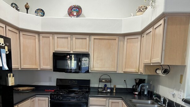 A kitchen with light wooden cabinets, a black stove, a microwave, and a sink. - Desert Oasis Retreat (Rio Rico)