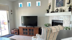 A living room with a television, a fireplace, a ceiling fan, and a patterned sofa. - Desert Oasis Retreat (Rio Rico)