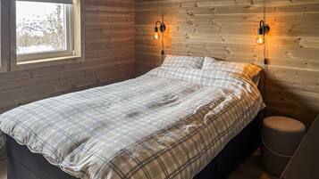 A bedroom with a bed, two wall-mounted light fixtures, a window, and a small round stool.