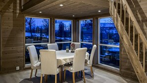 A dining area with a wooden table and chairs, large windows with a view of a snowy landscape, and a wooden staircase. - Cozy home in ålen with WiFi (Ålen)