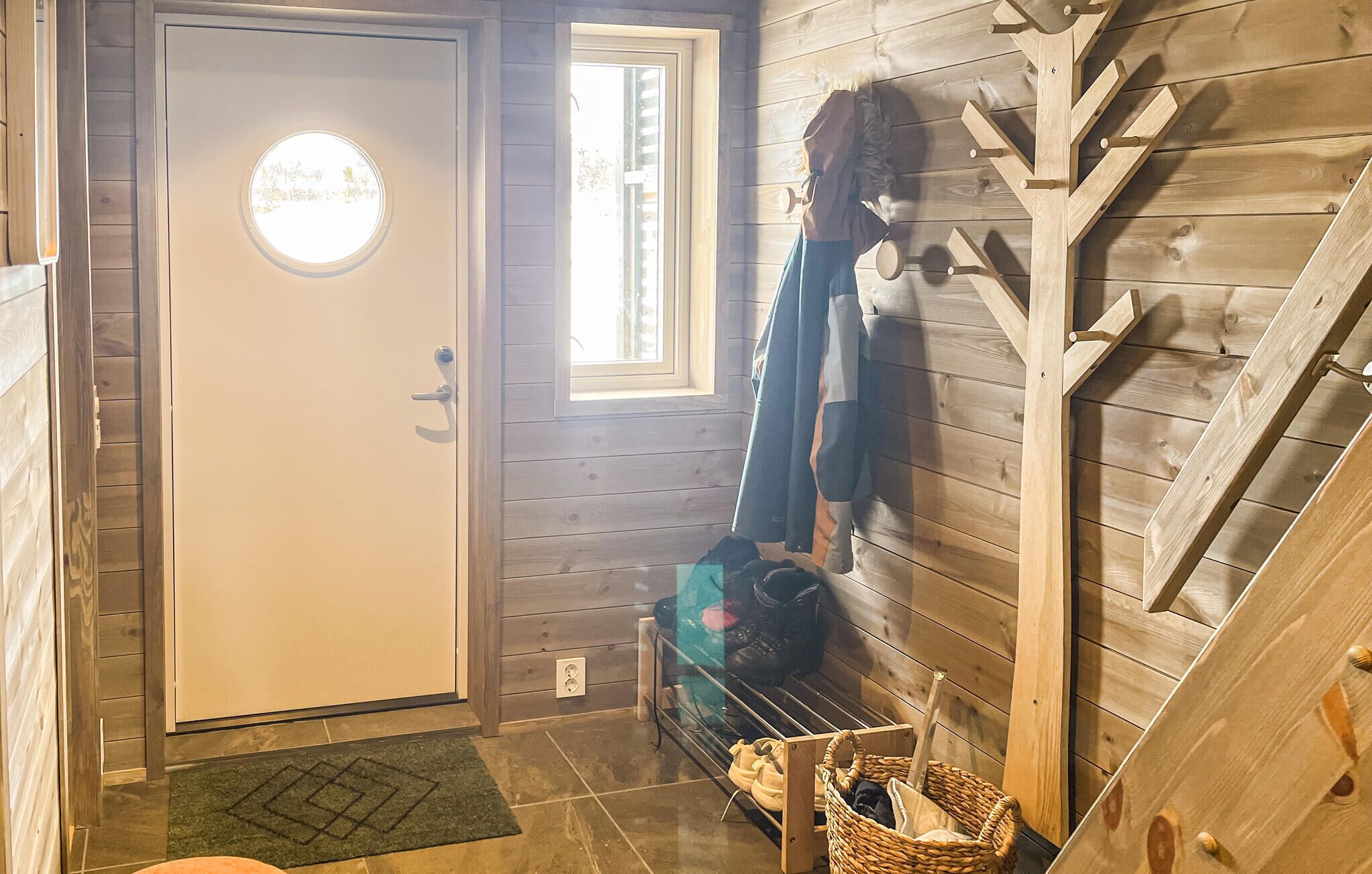 A wooden interior with a door, a window, a bench, and a coat rack.