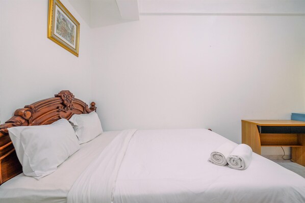 A neatly made bed with white linens and a wooden headboard, a wooden desk with a blue cushion, and a framed picture on the wall. - Cozy And Homey Studio Apartment At Margonda Residence 1 (Depok)