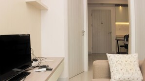 Un salon moderne avec un téléviseur à écran plat, une table basse en bois et un canapé beige agrémenté d’un coussin à motifs.