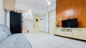 A modern living room with a grey sofa, a wooden accent wall, a television, and a kitchen area in the background. - Nice And Comfort 2Br Apartment At 30Th Floor M-Town Residence (Gading Serpong)