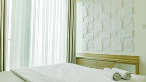 Ein Hotelzimmer mit einem ordentlich bezogenen Bett, einem Kopfteil mit geometrischem Muster und einem großen Fenster mit durchscheinenden Vorhängen.