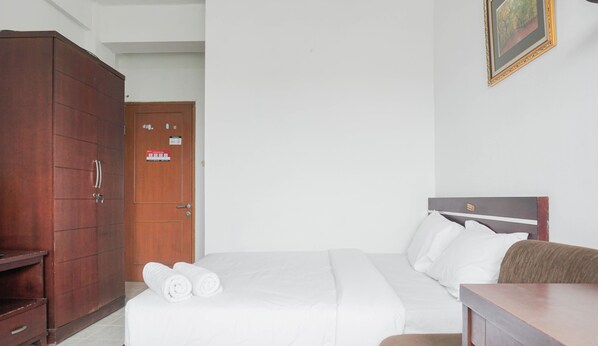 A hotel room with a bed, a wooden wardrobe, a door with a sign, and a framed picture on the wall.