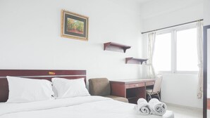 A hotel room with a bed, a desk, a chair, a window with curtains, and a framed picture on the wall. - Compact Studio At Margonda Residence 1 Apartment (Depok)
