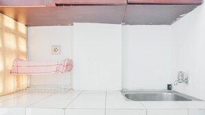 A kitchen with white tiles, a stainless steel sink, and a red checkered cloth hanging on a rack. - Compact Studio At Margonda Residence 1 Apartment (Depok)