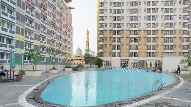 A swimming pool surrounded by multi-story residential buildings with balconies, a mosque with a green dome, and outdoor seating areas. - Compact Studio At Margonda Residence 1 Apartment (Depok)