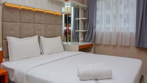 A hotel room with a large bed, white bedding, a wooden headboard, a bedside table, a mirror, and a window with curtains. - Comfortable 1Br At Signature Park Grande Near Cawang Station Apartment (Jakarta)