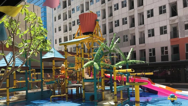 Un parque infantil con toboganes y estructuras para escalar, rodeado por una piscina.