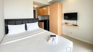 Una habitación de hotel con cama, televisión montada en la pared, zona de cocina y armario de madera.