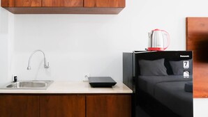 Una kitchenette compacta con un lavamanos, una cafetera y una caja negra sobre la encimera.